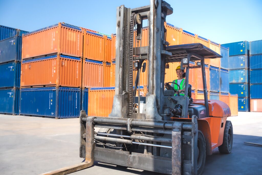 Woman driving forklift near shipping container.