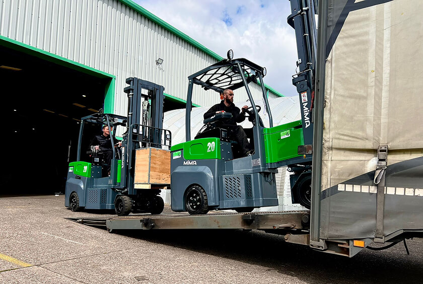Two MiMA forklifts being driven up ramp into back of a truck to place cargo inside