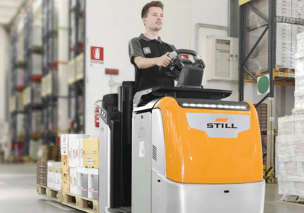 Man driving Still forklift inside a warehouse with pallets on the back and stock on the pallets